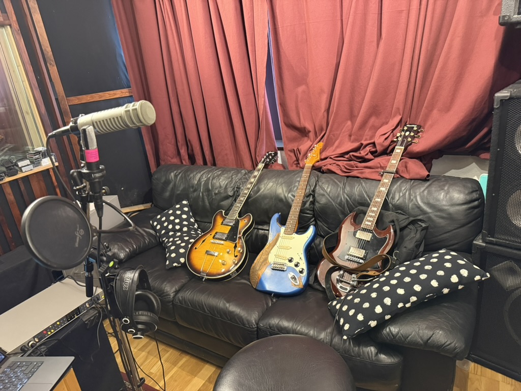 Gitarrer, mikrofon och inspelningsutrustning framför studiosoffan